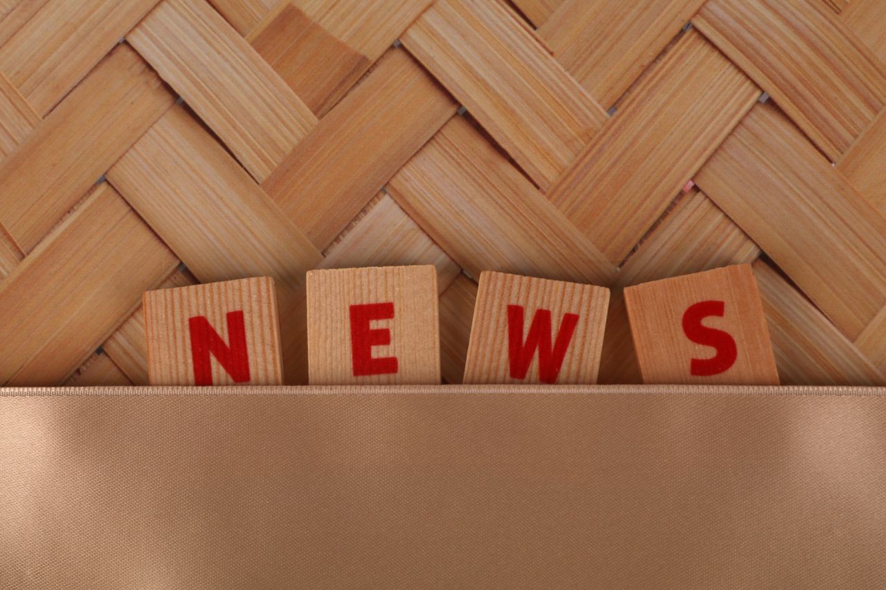 Wooden blocks spelling 'NEWS' against a woven pattern background with ample copyspace.